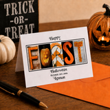 a Halloween-themed greeting card with the word "FORST" spelled out in the shape of a pumpkin and other Halloween-related elements. The card is placed on a wooden surface, with a pumpkin and a pen nearby.