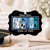A black ornament with musical notes and a graduation cap, placed on a table with a vase of white flowers and books.