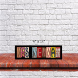 A wooden shelf against a white brick wall, with a sign that says "MRS NEWMAN" made up of colorful letters.