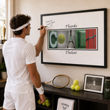 A man in a white shirt is writing on a framed picture that says "Thanks Coach!" in a room with various tennis-related items, such as a tennis racket, tennis balls, and a framed photograph of a tennis player.