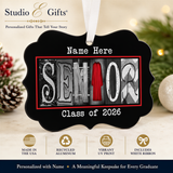 The image is a personalized graduation ornament with the name "Name Here" and the word "SENIOR" made of letters. The ornament is hanging on a wall and is described as a "RECYCLED ALUMINUM" and "VIBRANT UV PRINT" ornament. It is also referred to as a "CLASS OF 2026" ornament. The ornament is made in the USA and includes a "WHITE RIBBON" ribbon. The image is a collage of various images, and the text describes the ornament as a "Meaningful Keepsake for Every Graduate".