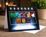 A greeting card with various icons and symbols related to music and entertainment, such as a piano, microphone, ticket, and stage, displayed on a wooden surface.