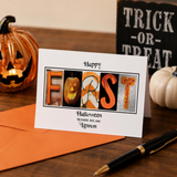 A Halloween-themed greeting card with the word "FORST" spelled out in the shape of a pumpkin and other Halloween-related images. The card is placed on a wooden surface, with a pumpkin and a Halloween sign visible in the background.